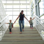 twin toddlers walking down stairs holding mom's hands