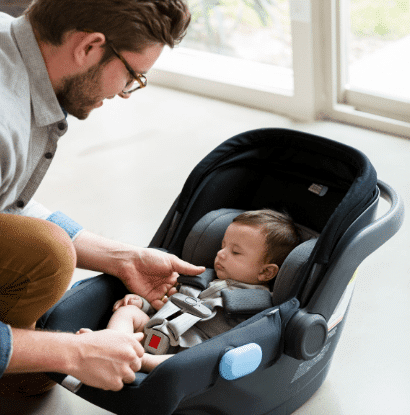 man buckling baby in car seat