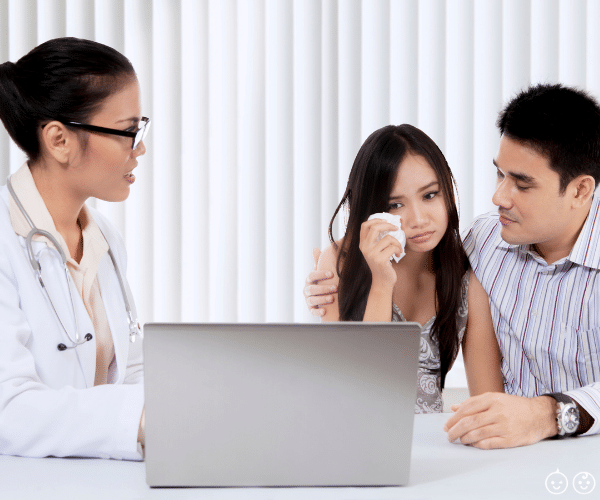 a doctor showing a couple a computer screen. the man has his arm around the woman who is holding a tissue, grieving her miscarriages