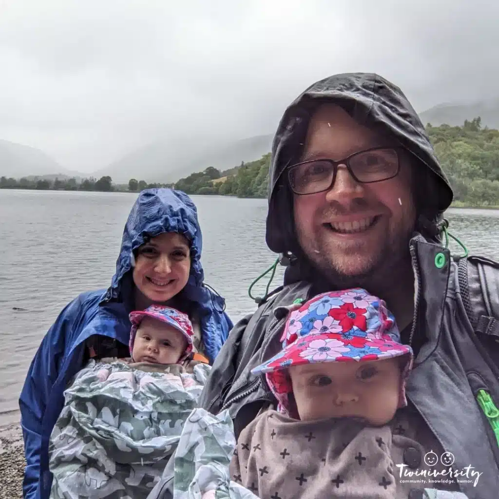 Mom and dad each holding a baby and standing infront of a large body of water